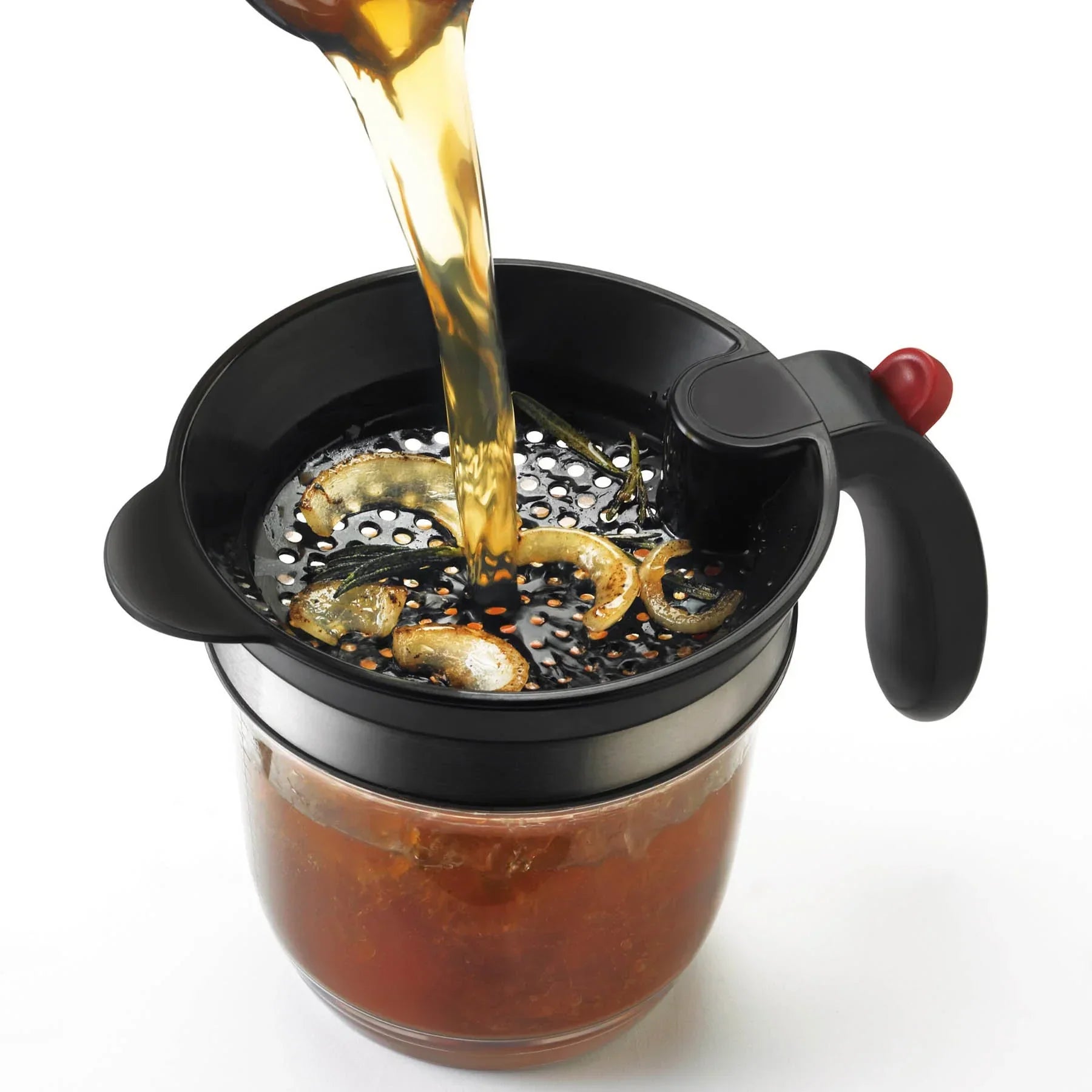 Black metal cocktail strainer with lemon and herbs straining brown liquid into glass jar