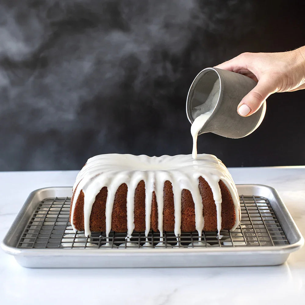 Hand pouring white icing over classic fluted loaf cake on wire rack in baking tray