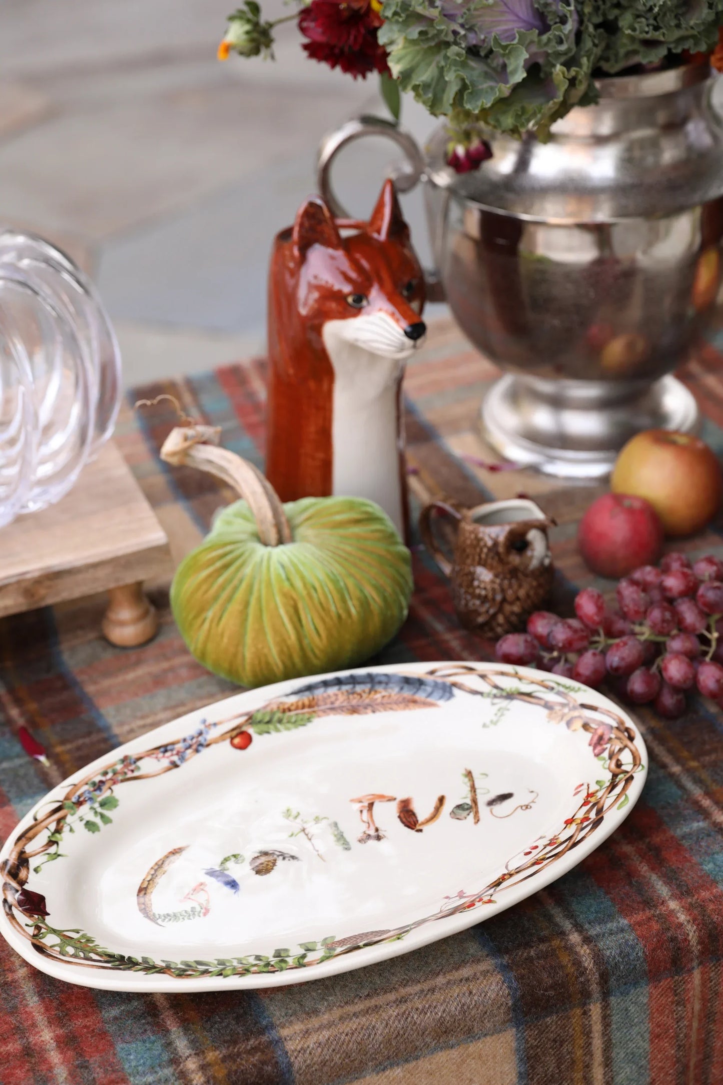 Autumn table setting with a gratitude plate, velvet green pumpkin, ceramic fox and owl pitchers, grapes, and apples
