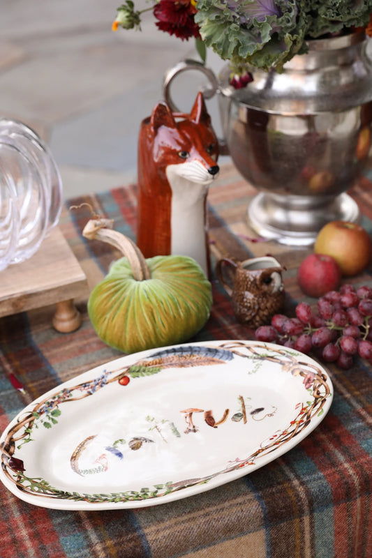 Autumn table setting with a gratitude plate, velvet green pumpkin, ceramic fox and owl pitchers, grapes, and apples