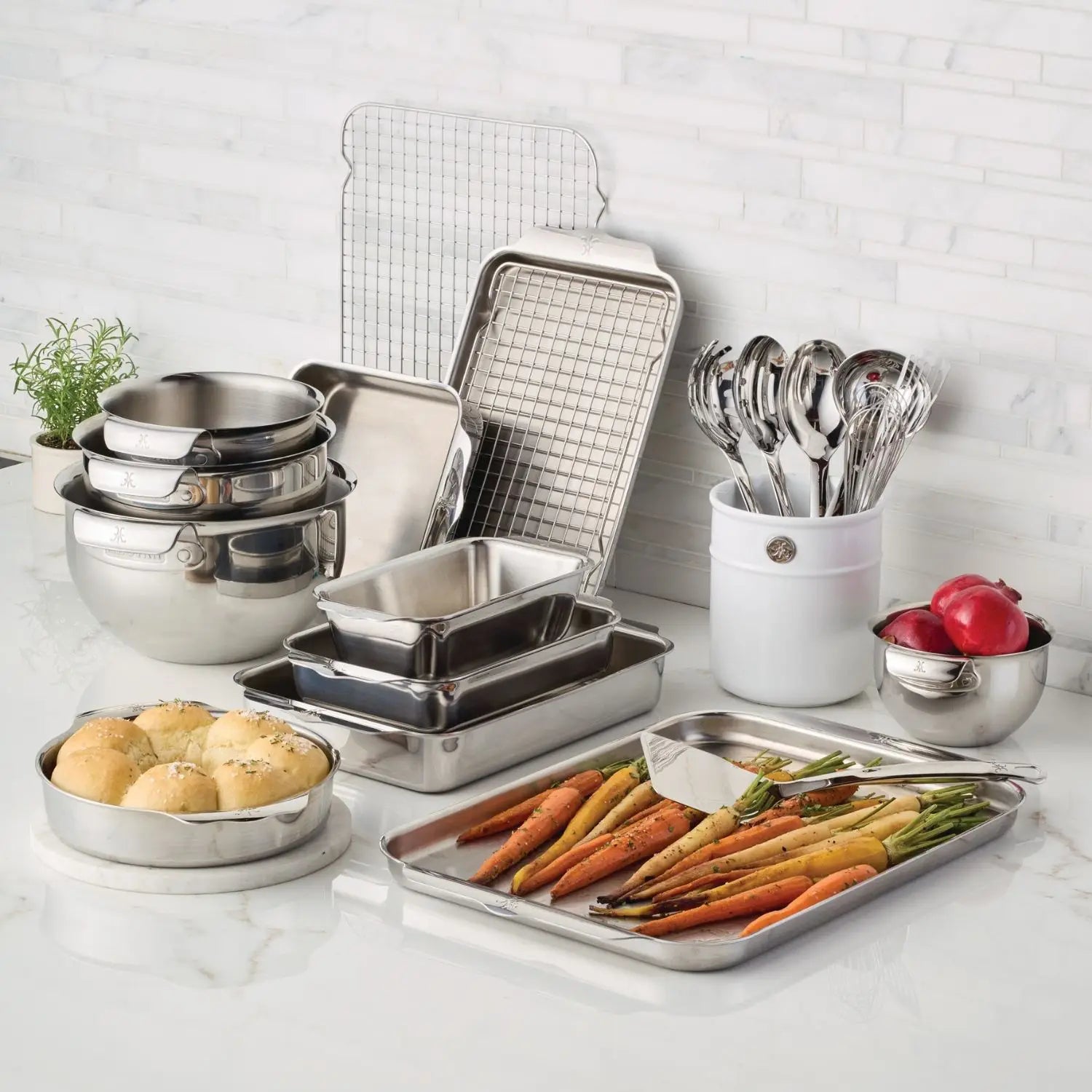 Collection of Hestan Oven Bond stainless steel kitchen utensils and cookware on a white countertop.