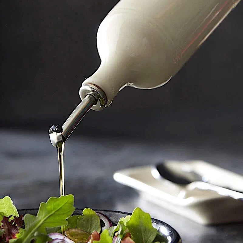 White ceramic oil cruet pouring olive oil over fresh mixed green salad in black bowl