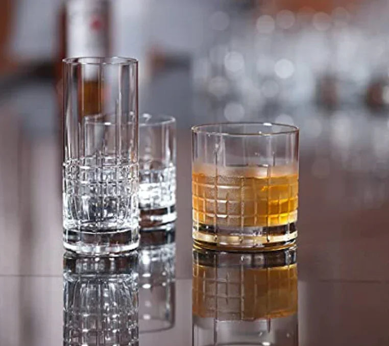 Set of three textured whiskey glasses on reflective surface, one glass with amber whiskey and ice