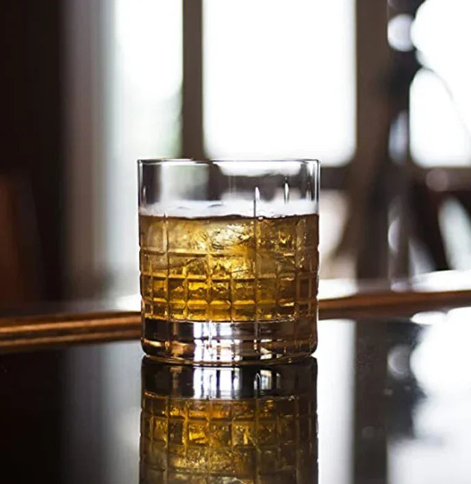 Whiskey glass with ice cubes on shiny black surface with blurred background