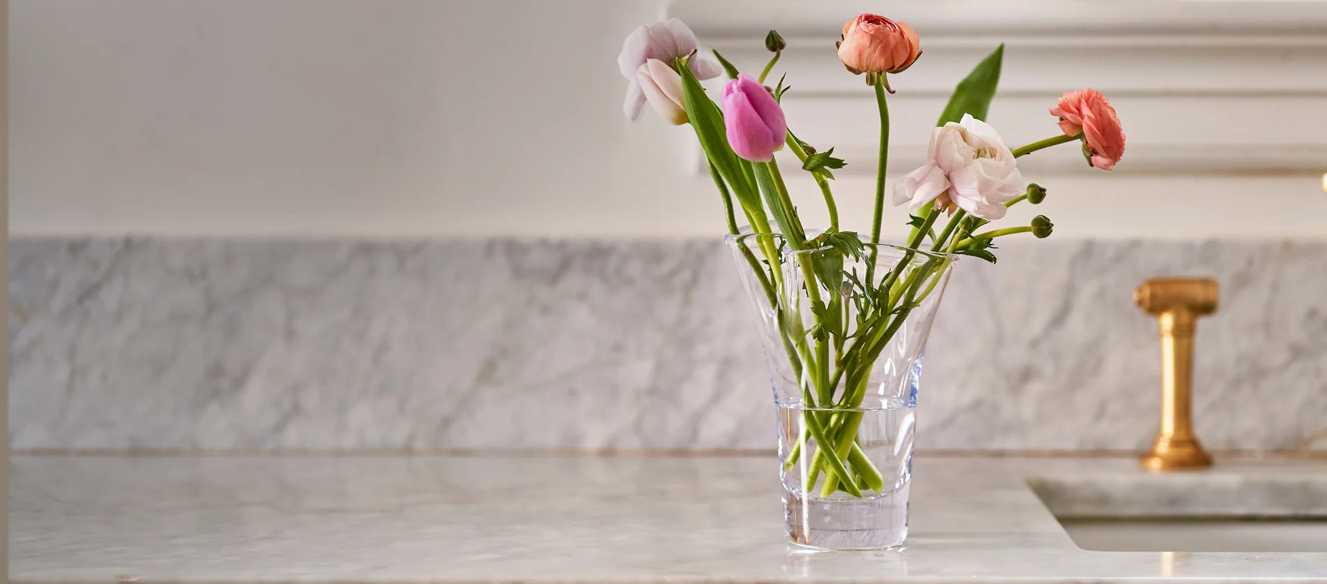 Simon Pearce Clear glass vase with pink flowers on a kitchen counter