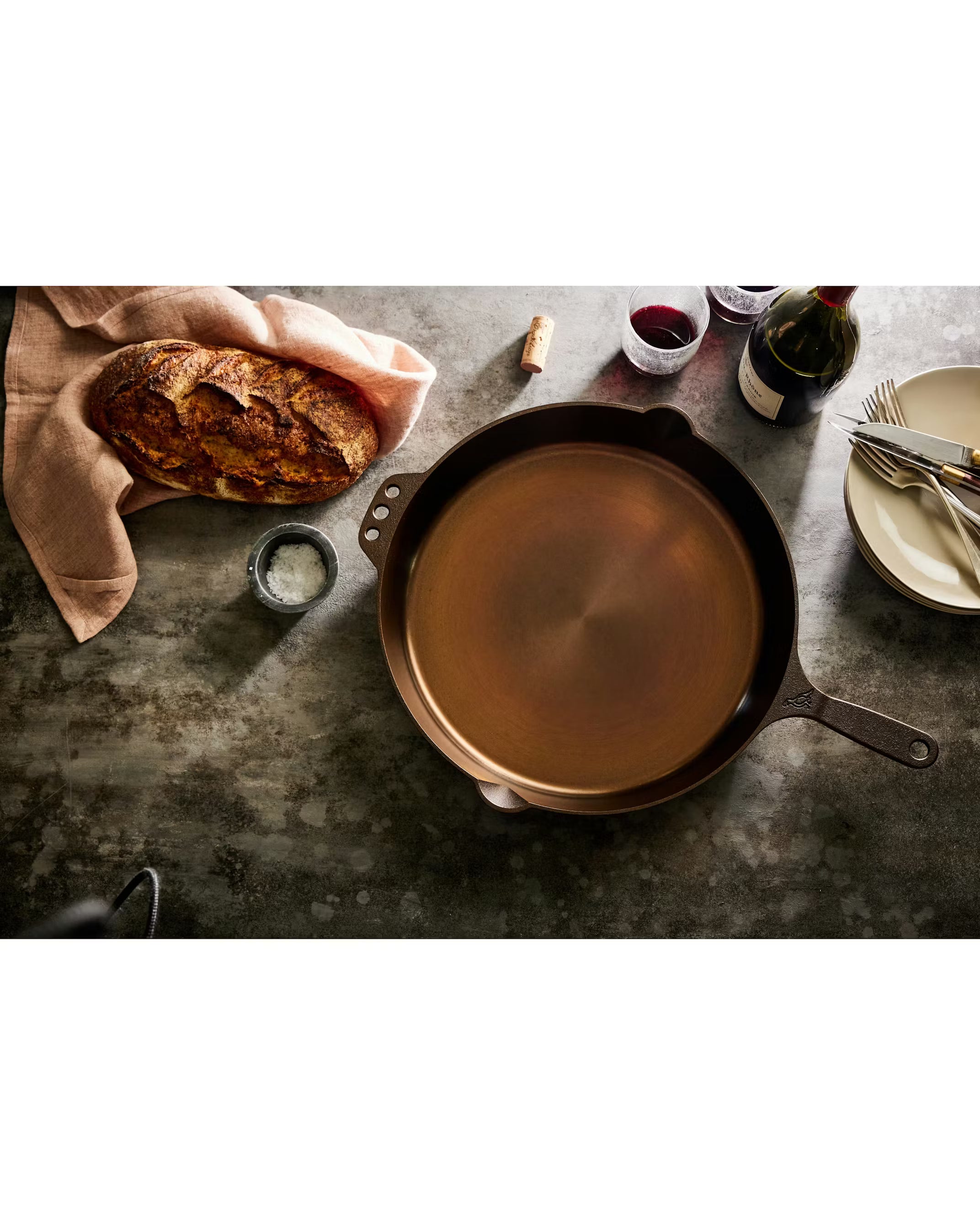 Smithey Cast iron skillet with a brown liquid on a rustic table setting with bread and wine.