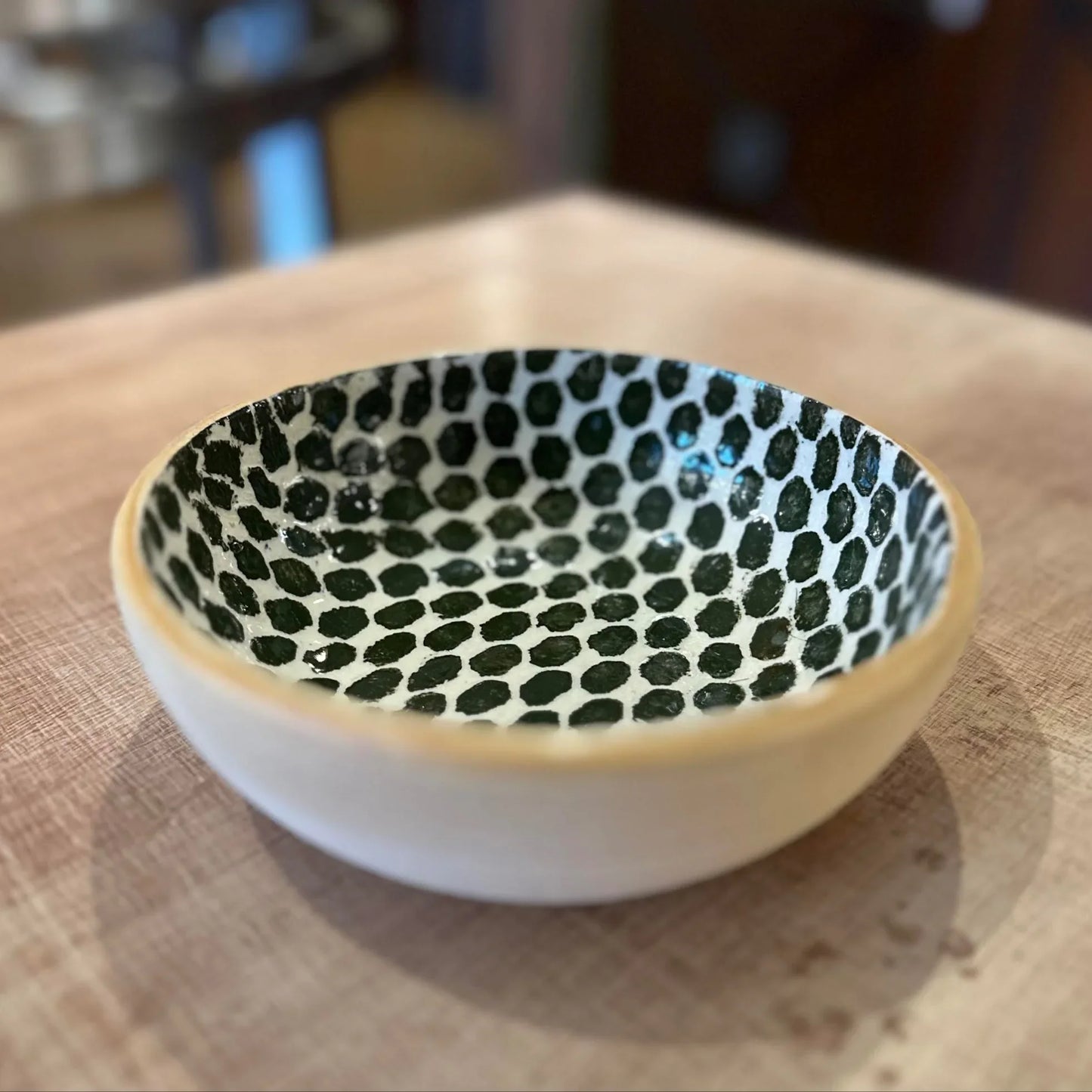 Small ceramic bowl with dark green dot pattern on a wooden surface