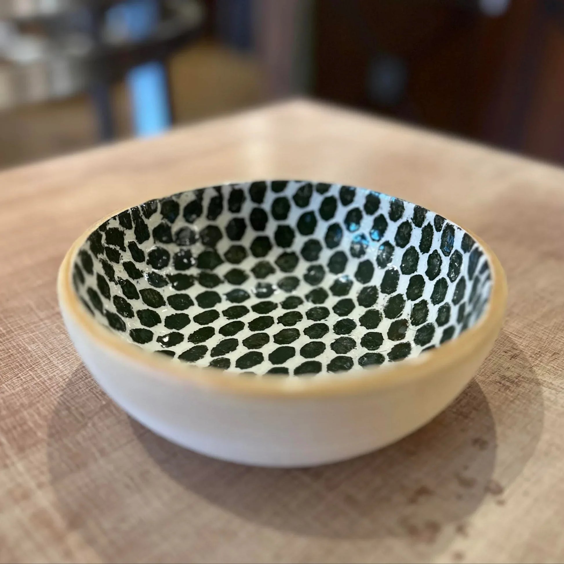Small ceramic bowl with dark green dot pattern on a wooden surface