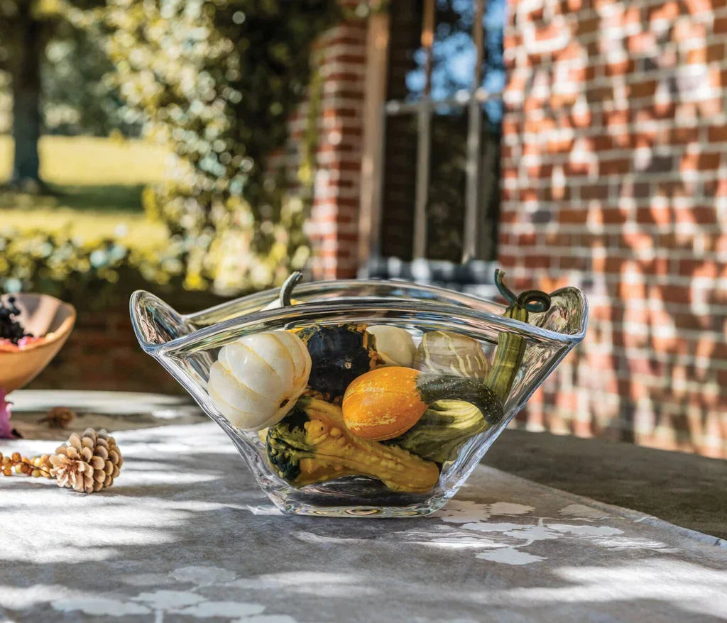 Clear glass decorative bowl with mixed gourds on outdoor table with brick wall background