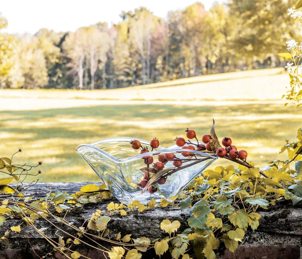 Clear glass decorative bowl with red berries on old stone wall with green and yellow foliage in a sunlit field