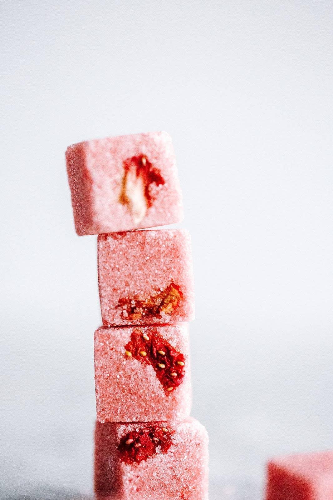 Stack of four pink sugar-coated Turkish delight cubes with embedded dried rose petals against a white background