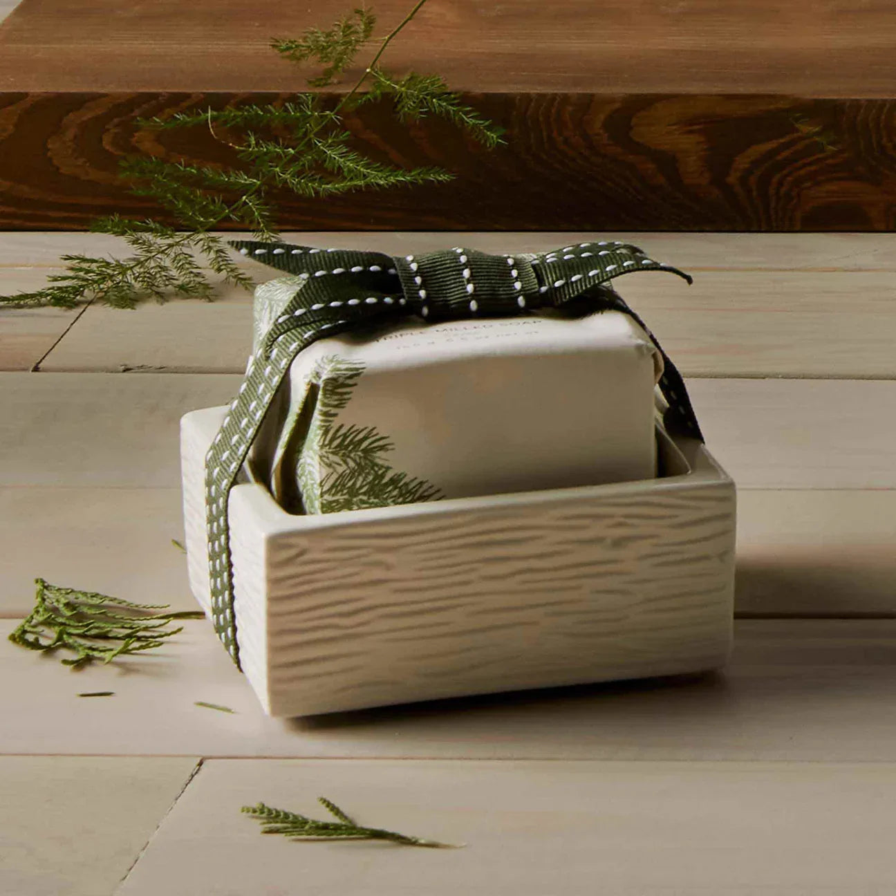 Ceramic soap dish with wrapped bar soap tied with green ribbon on rustic wooden surface
