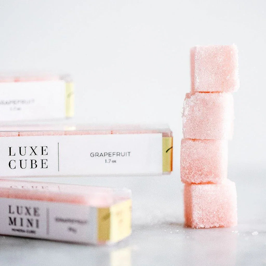 Stack of four pink grapefruit flavored sugar cubes with Luxe Cube packaging on white background