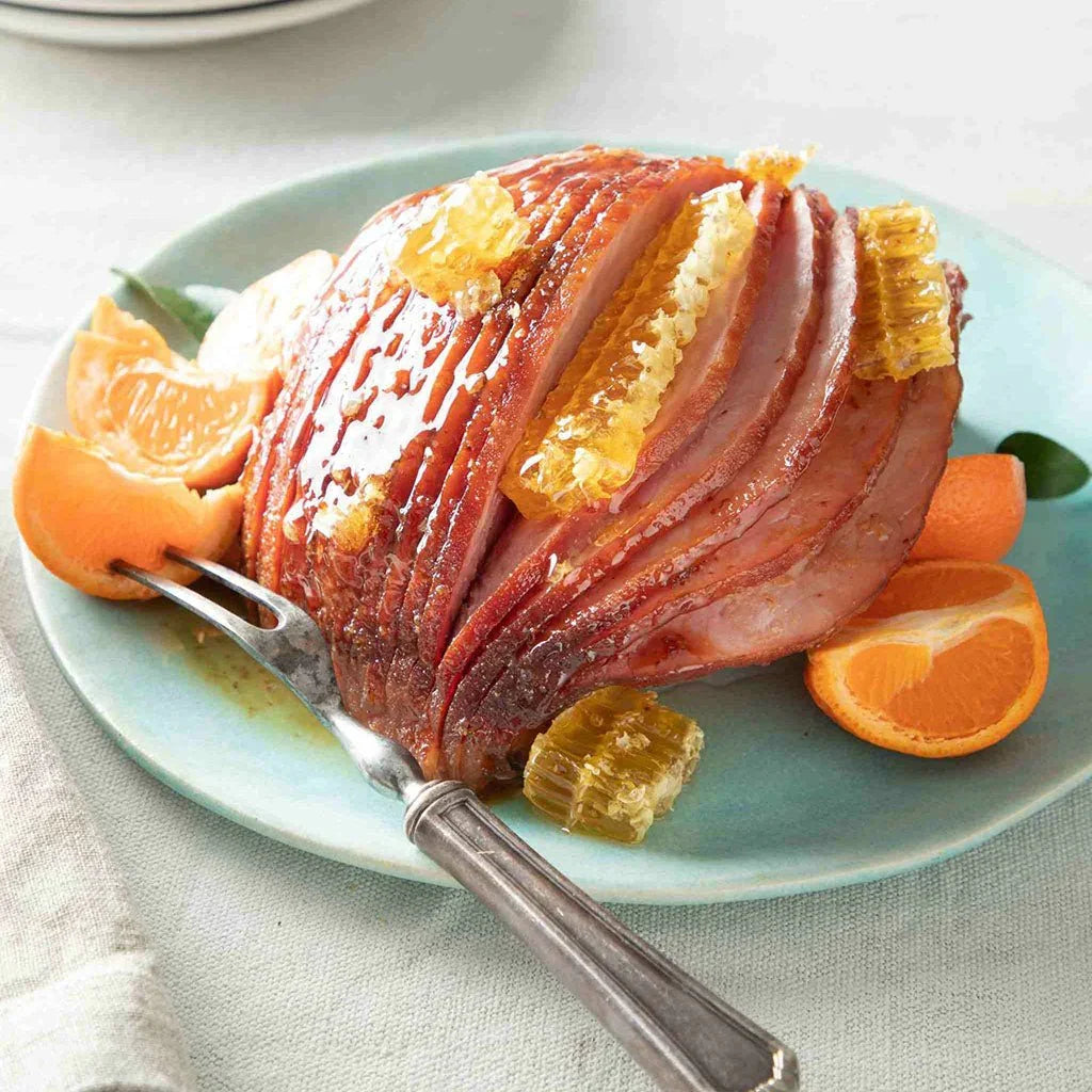 Sliced glazed ham with honeycomb pieces on blue plate garnished with orange wedges