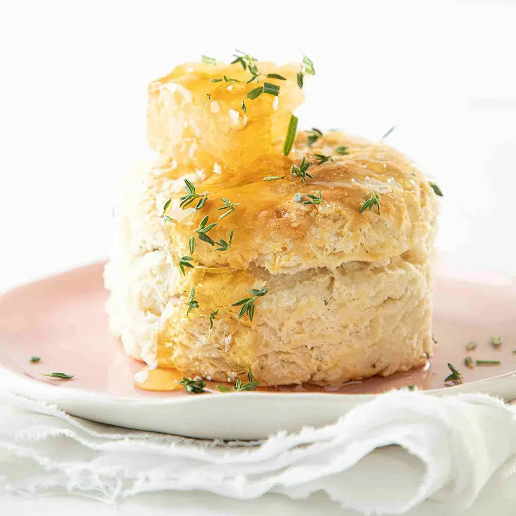 Fluffy biscuit topped with honeycomb, honey drizzle, and fresh thyme on a pink plate