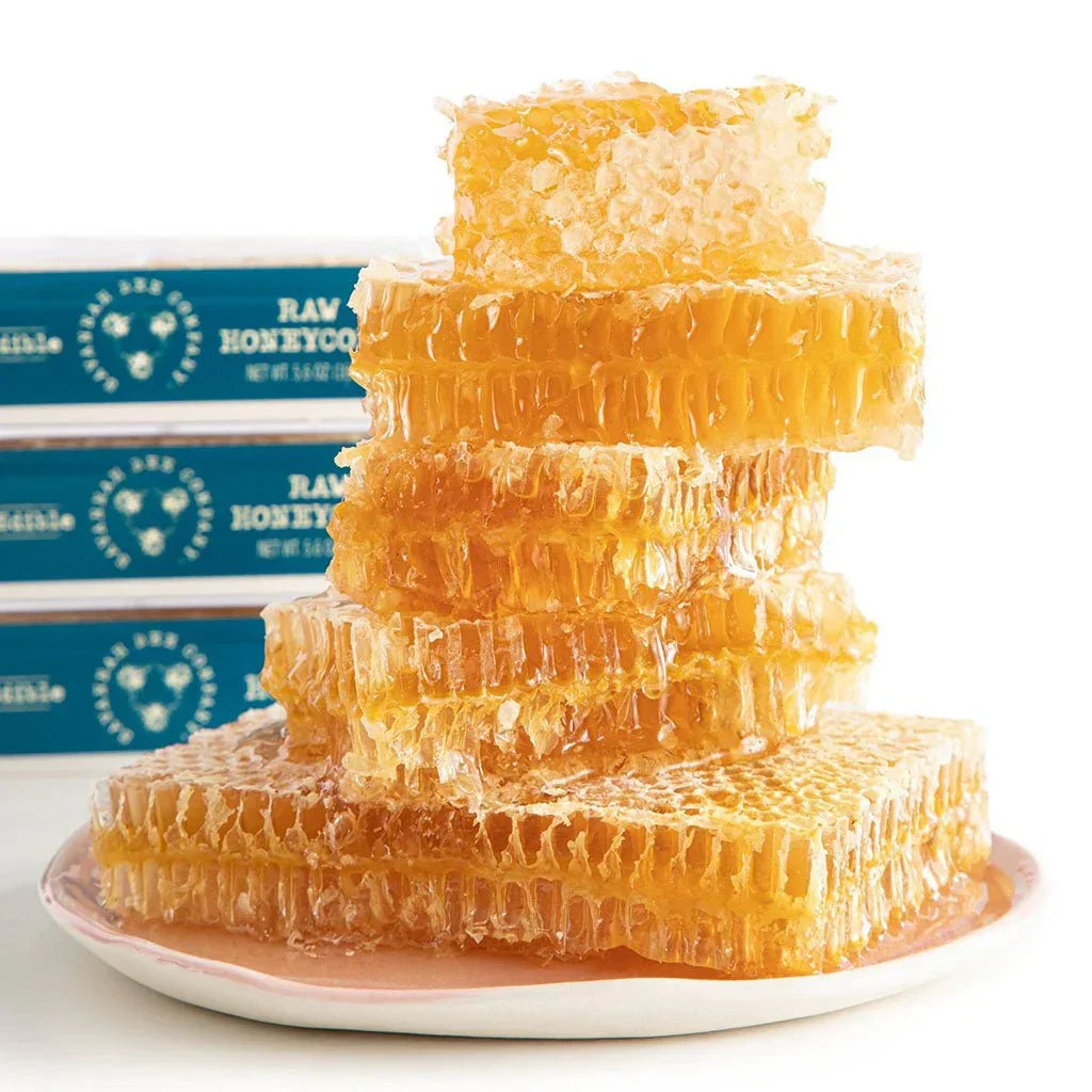 Stack of raw honeycomb pieces dripping honey on a plate with packaged honeycomb in the background
