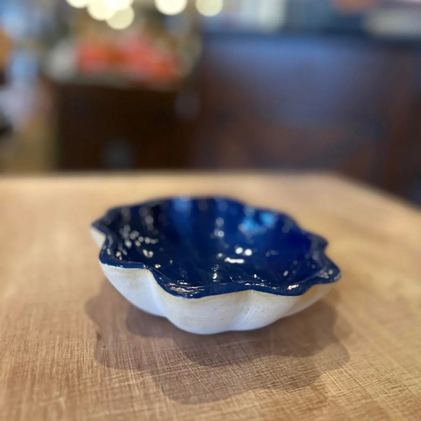 Small scallop-shaped ceramic bowl with deep blue glazed interior and white exterior on wooden surface