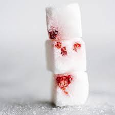Three stacked white ice cubes with red fruit pieces inside on a light surface