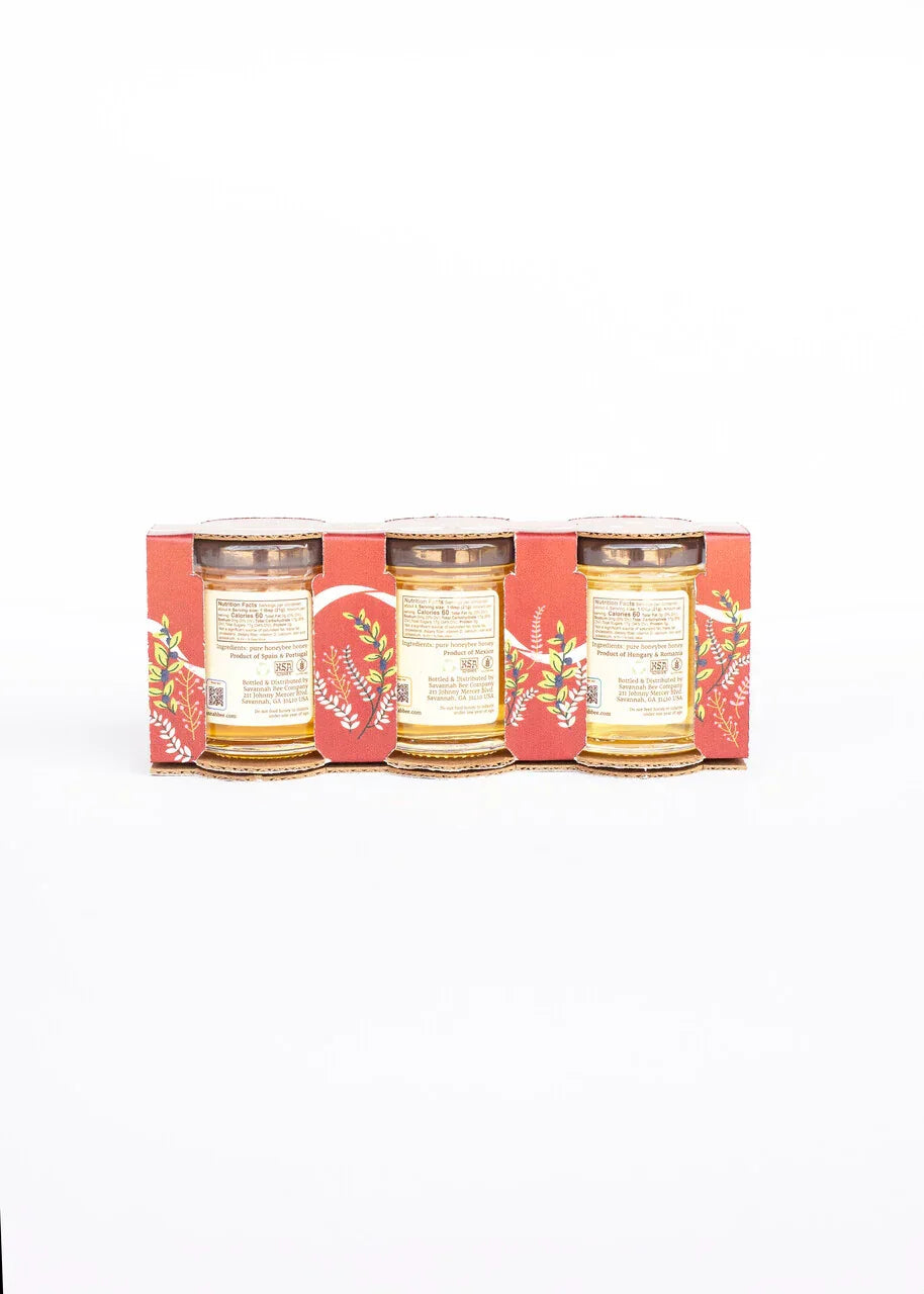 Three-pack of small honey jars in red floral cardboard packaging with nutrition labels