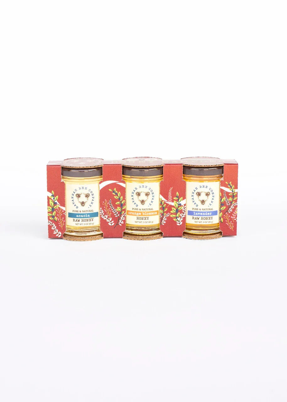 Three jars of Savannah Bee Company raw honey in acacia, orange blossom, and lavender flavors in decorative red packaging