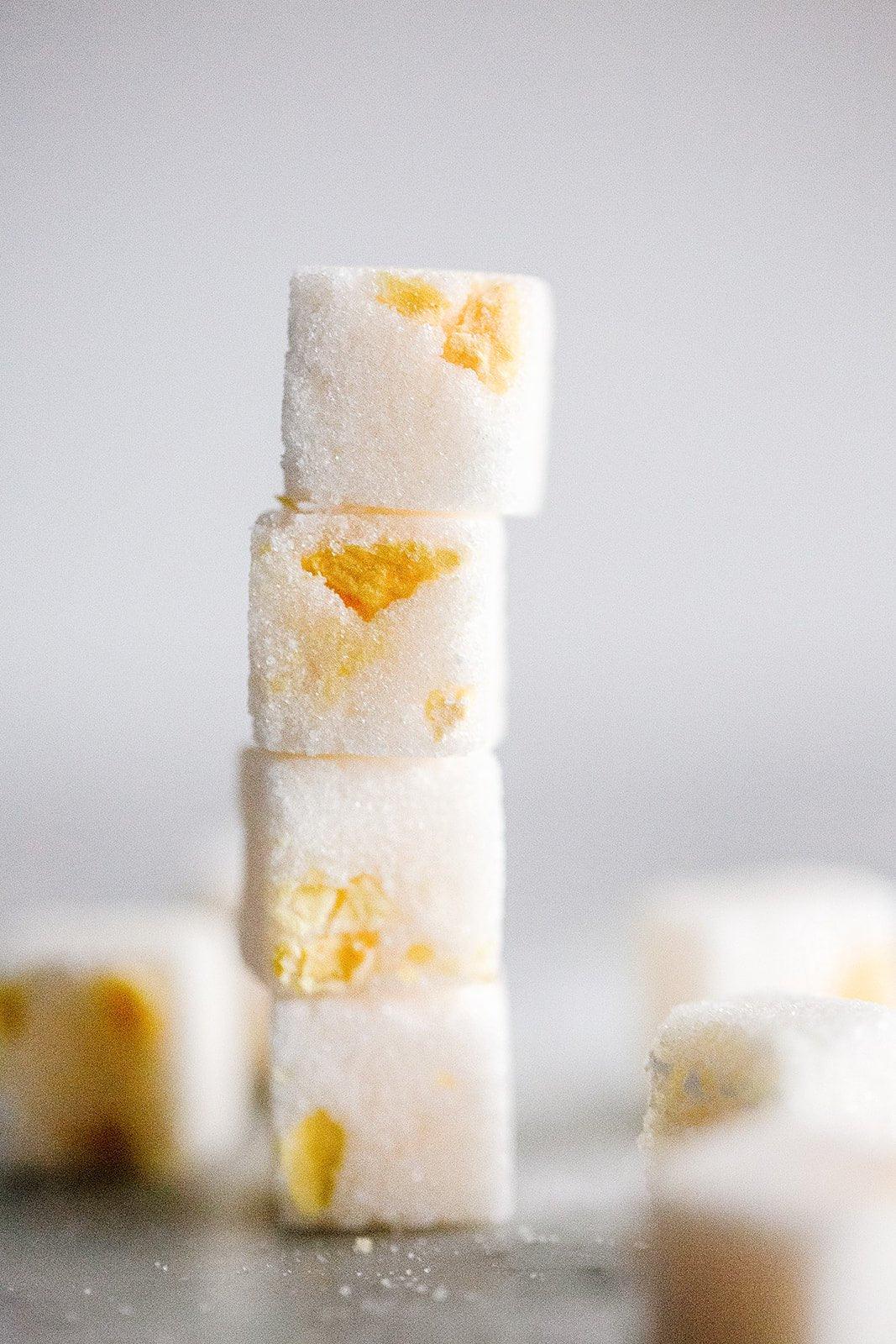Close-up of stacked white sugar cubes with yellow peach pieces inside on a blurred gray background