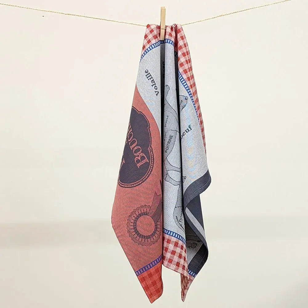 Red and blue French jacquard cotton kitchen towel with butchery and meat cut illustrations hanging on a clothespin