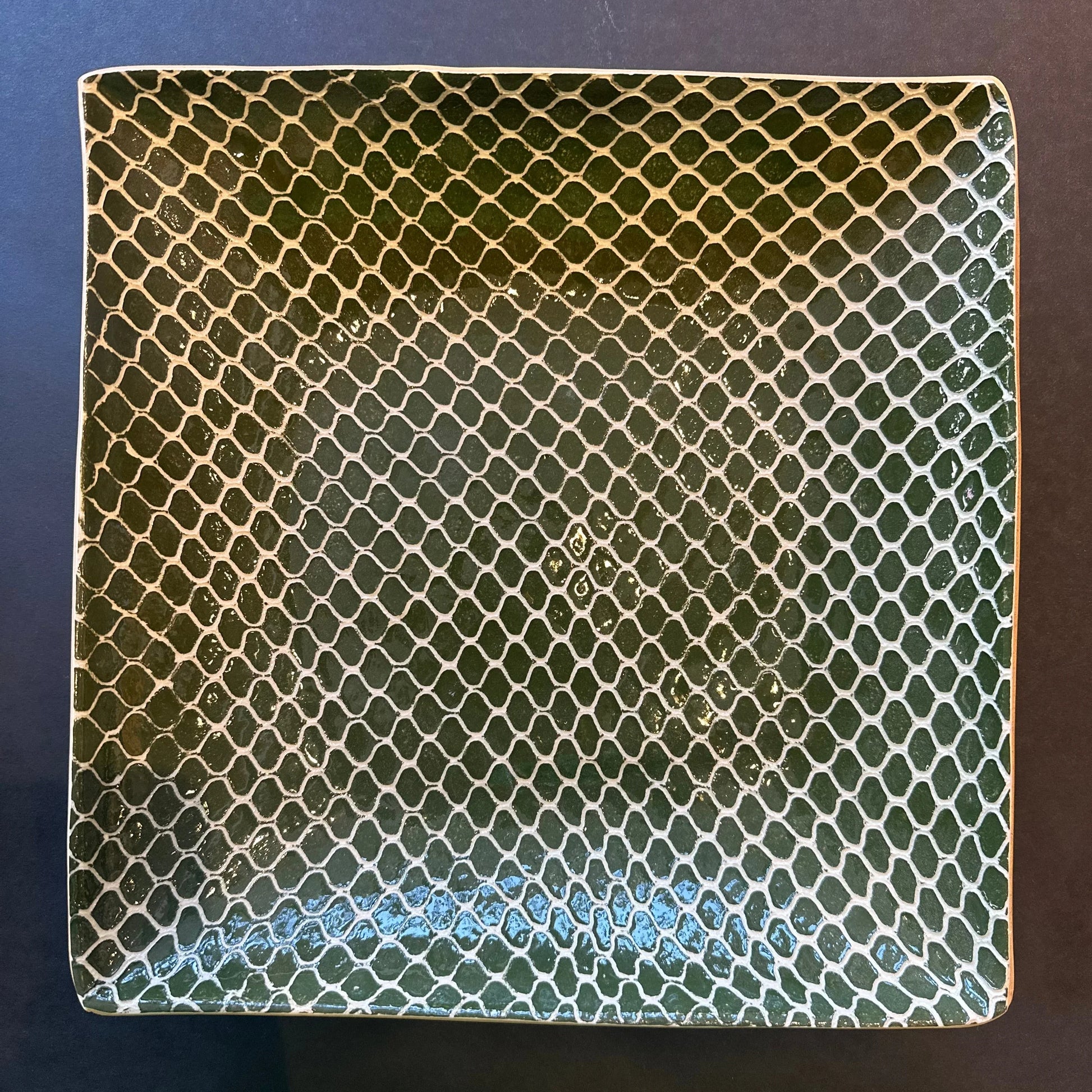 Square ceramic tile with a green and white pattern on a dark background
