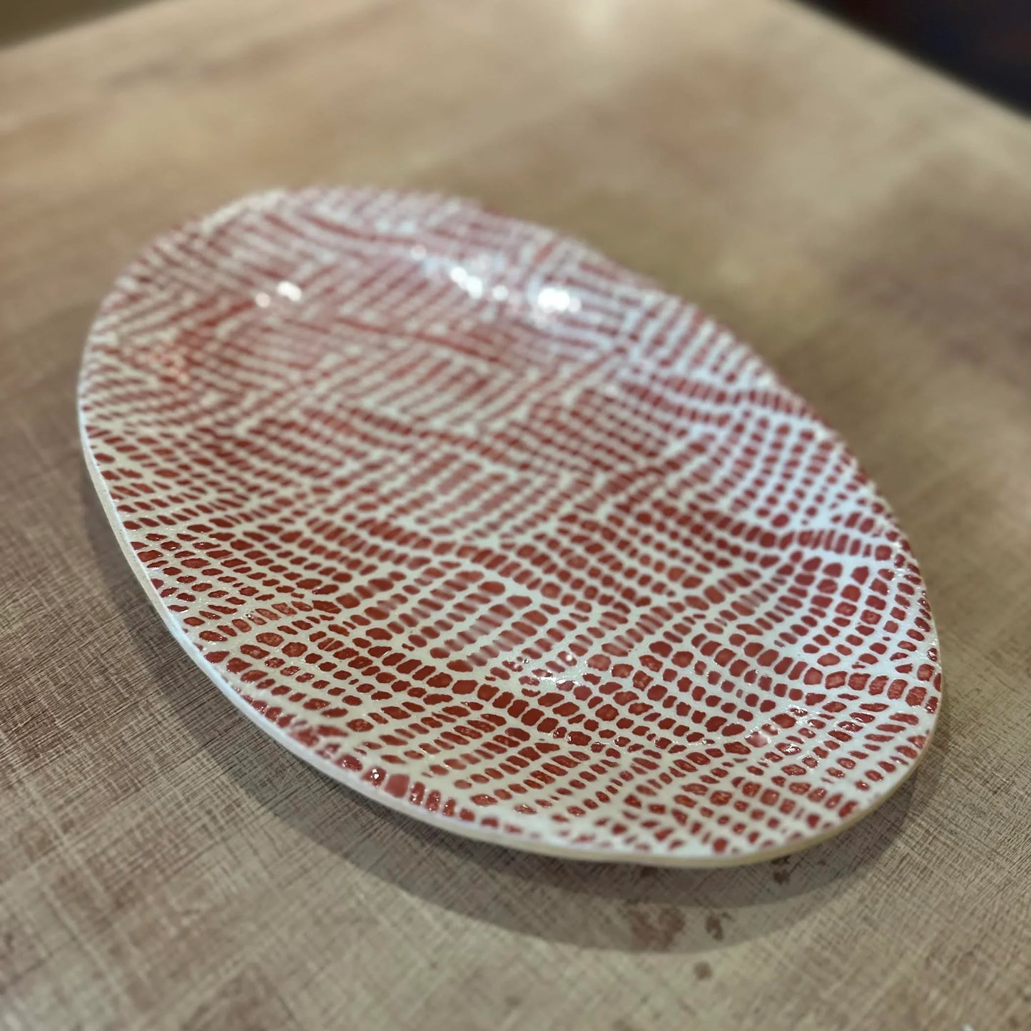 Oval ceramic plate with rust red pattern on a wooden surface