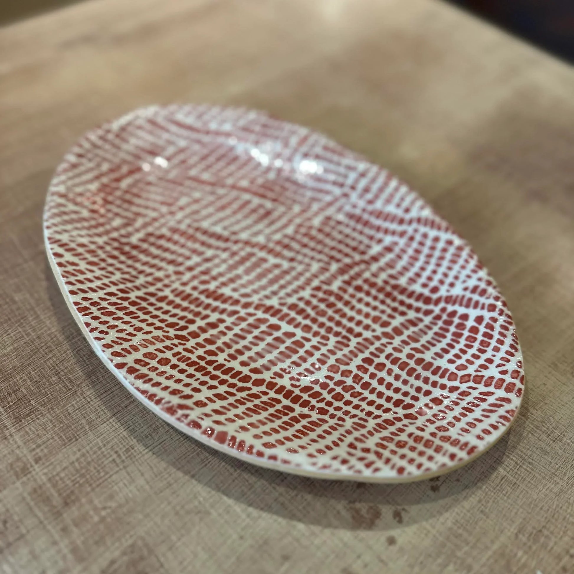 Oval ceramic plate with rust red pattern on a wooden surface