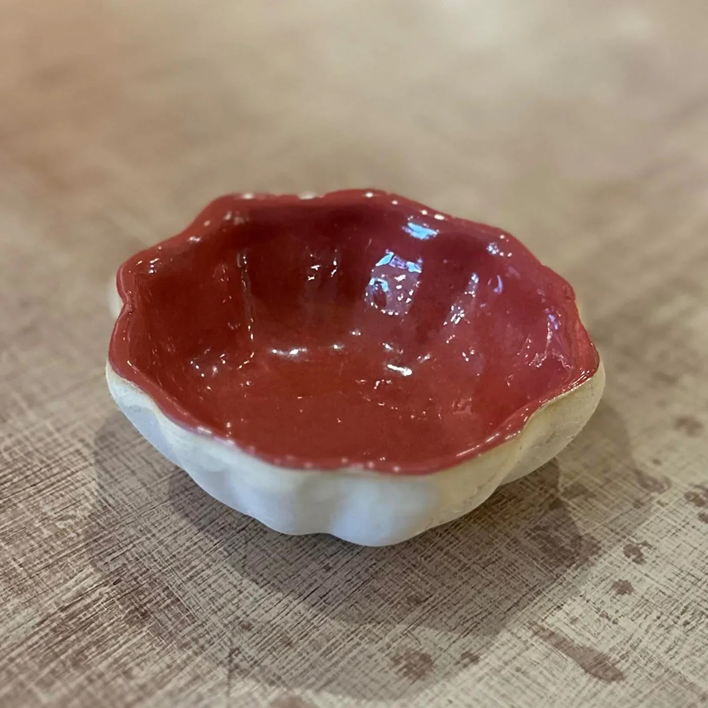 Small ceramic bowl with wavy edge and red interior on a textured surface