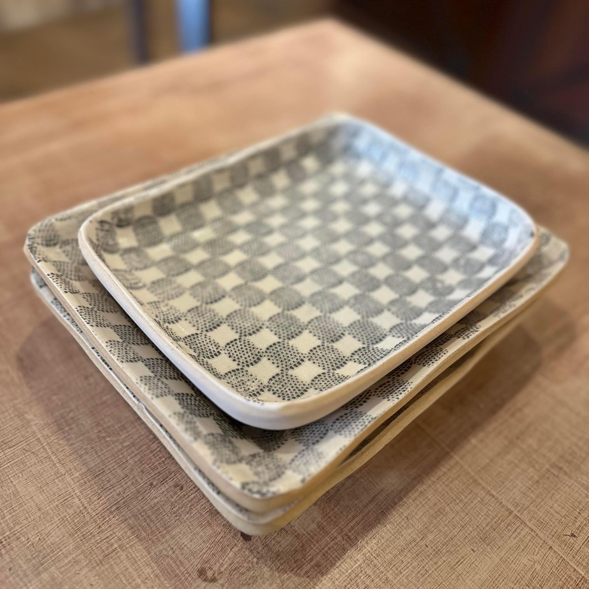 Stack of rectangular ceramic trays with checkered pattern on a wooden surface