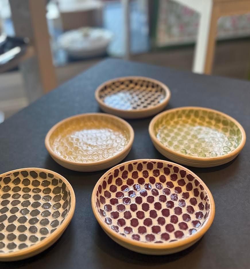 Set of five handmade ceramic coasters with colorful polka dot patterns on a black table